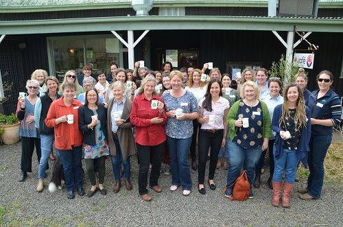 Women's Network gather in front of a country cafe, raising their Country Cuppas-branded mugs