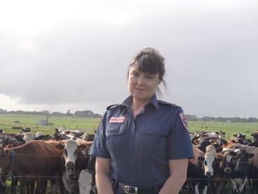 Ambulance Victoria volunteer Andrea Vallance stands in a field in front of a herd of cows