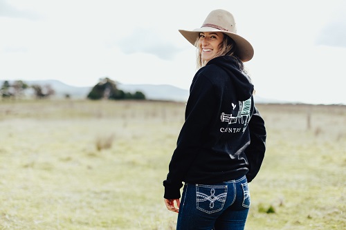 Entrepreneur Megan Lawrence stands in a field wearing one of her navy hoodies from her online clothing business