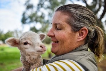 Farmer Carly Noble holds a newborn lamb in the paddock