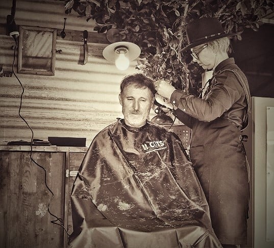 Hairdresser giving haircut in woolshed style mobile barber shop