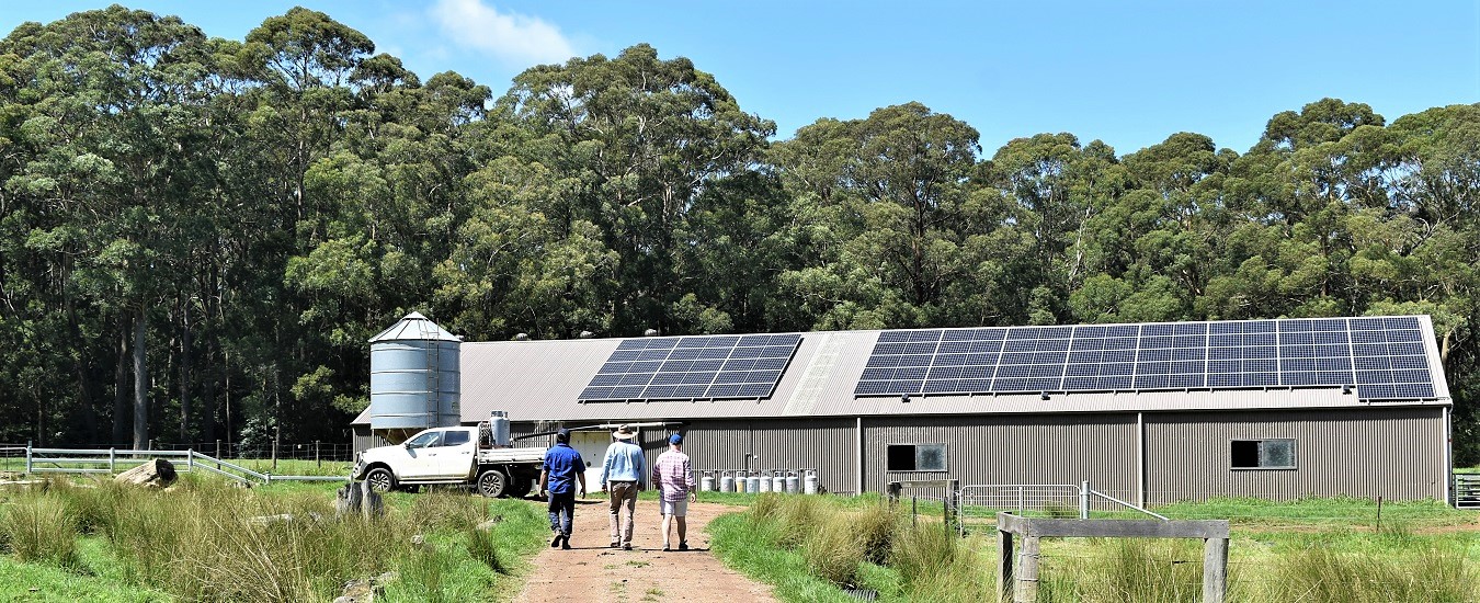 Dairy farm shed with solar panels farm vehicle blue sky and three people on dirt track