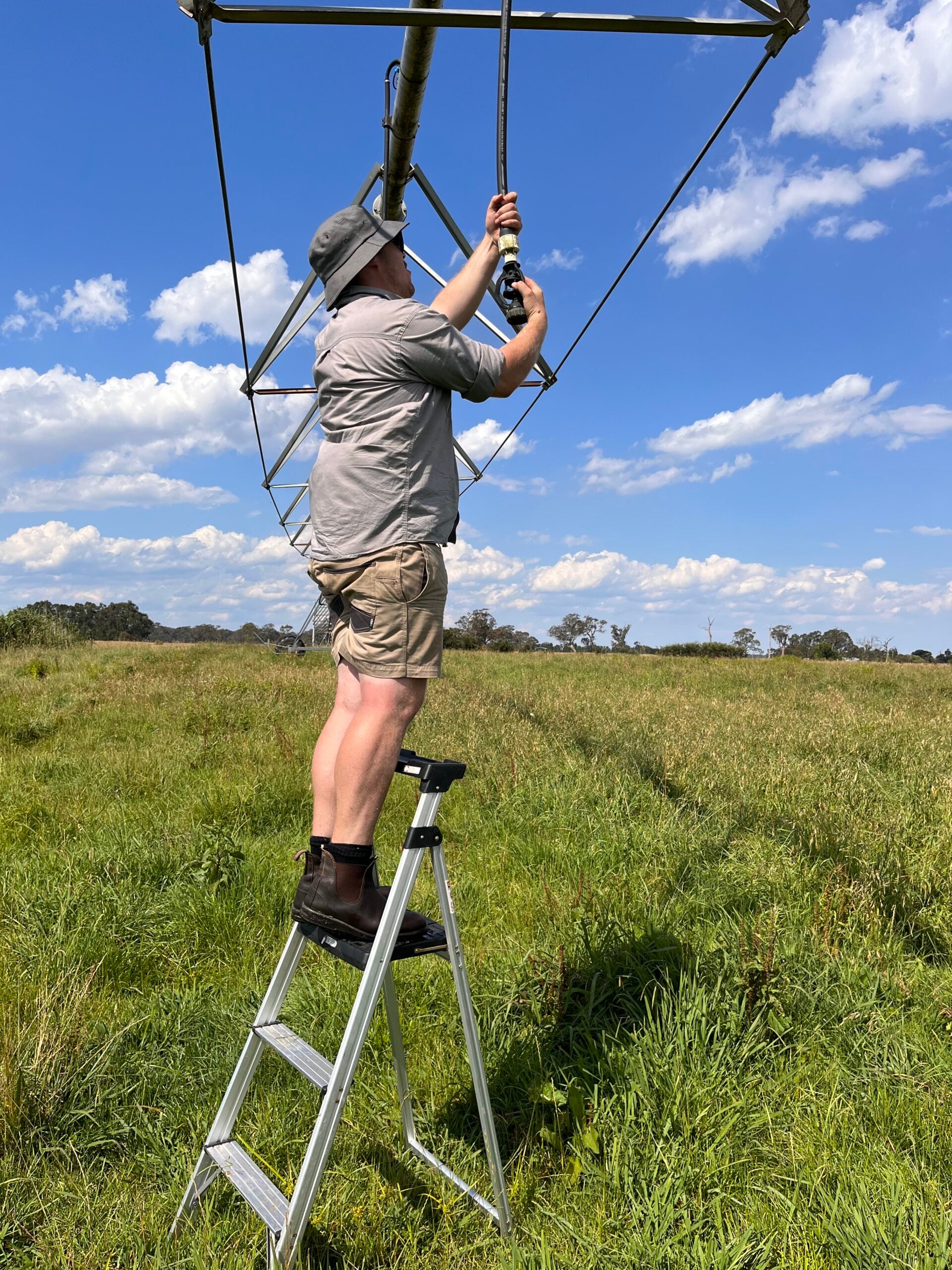 Man on ladder tending to sprinklers on centre pivot in a field of pasture